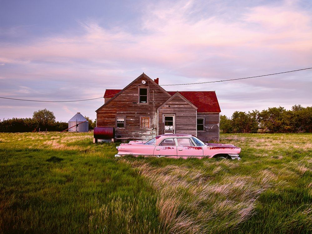 An abandoned pink car in front of a wooden house
