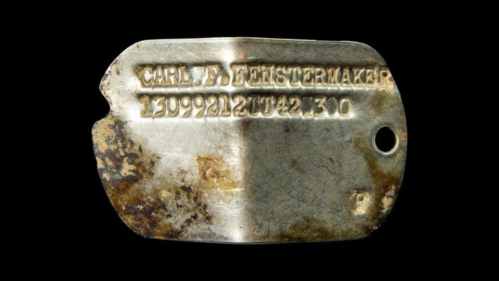 Small metal plate engraved with name and number, shaped like a dog tag
