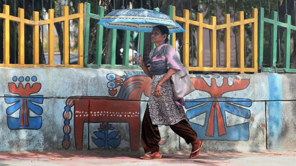A woman walks under the shelter of an umbrella during the intense heat in New Delhi, India