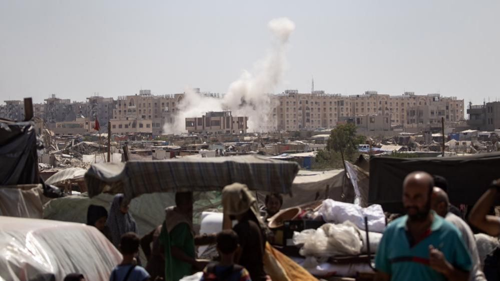 People flee as smoke rises amid the advance of Israeli military vehicles in an area sheltering internally displaced Palestinians, in Khan Younis, southern Gaza Strip, 18 August 2024.