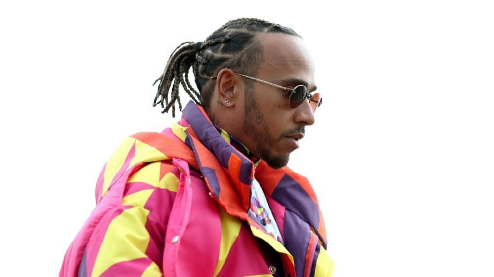 Lewis Hamilton with long dark hair wearing a multicoloured jacket