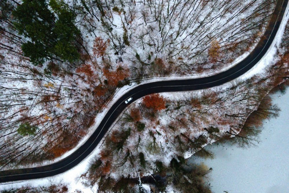 A picture taken with a drone shows a car moving slowly through a snow-covered forest near Sikonda, Hungary
