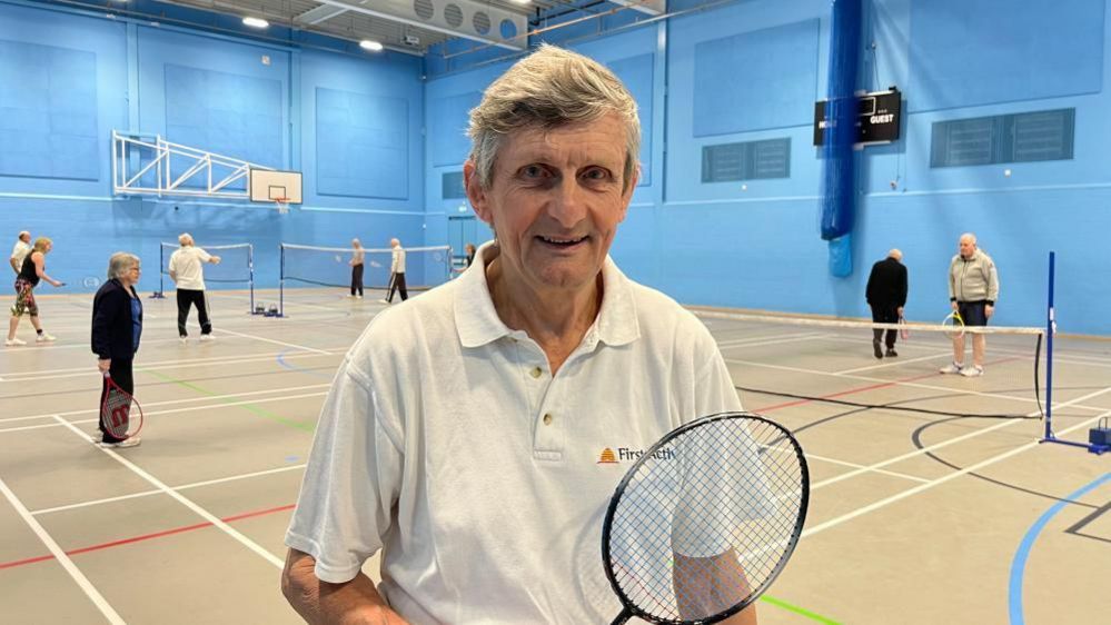 Ray Howes standing with a tennis racquet inside a sports hall