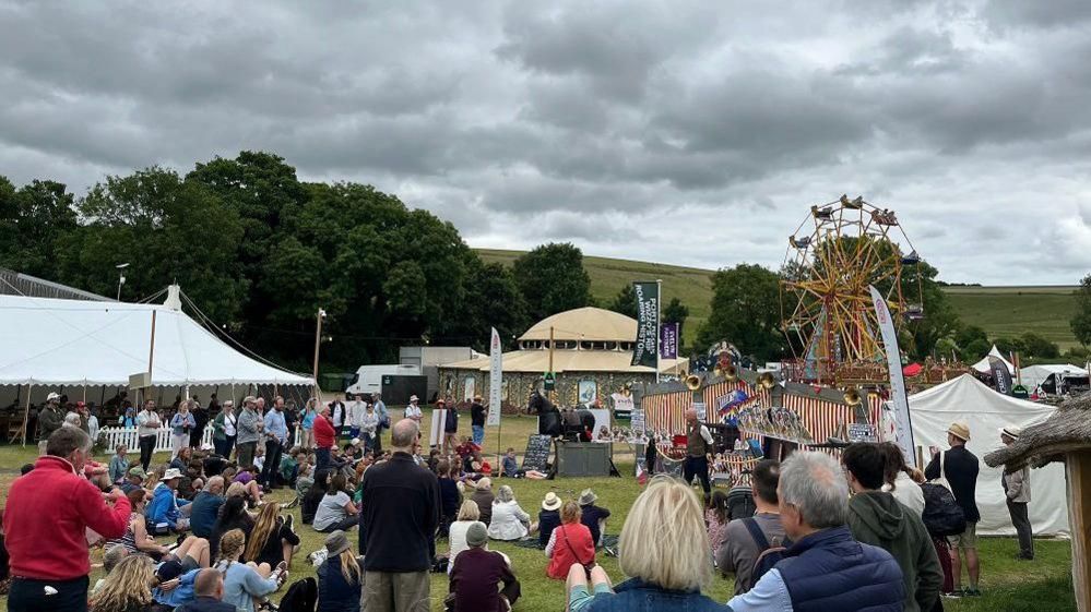 A crowd gathers round an outdoor demonstration at the festival, with marquees round as well