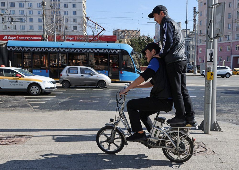 Two work migrants from Kyrgyzstan ride bicycle on the street, April,14,2023, in Moscow, Russia.