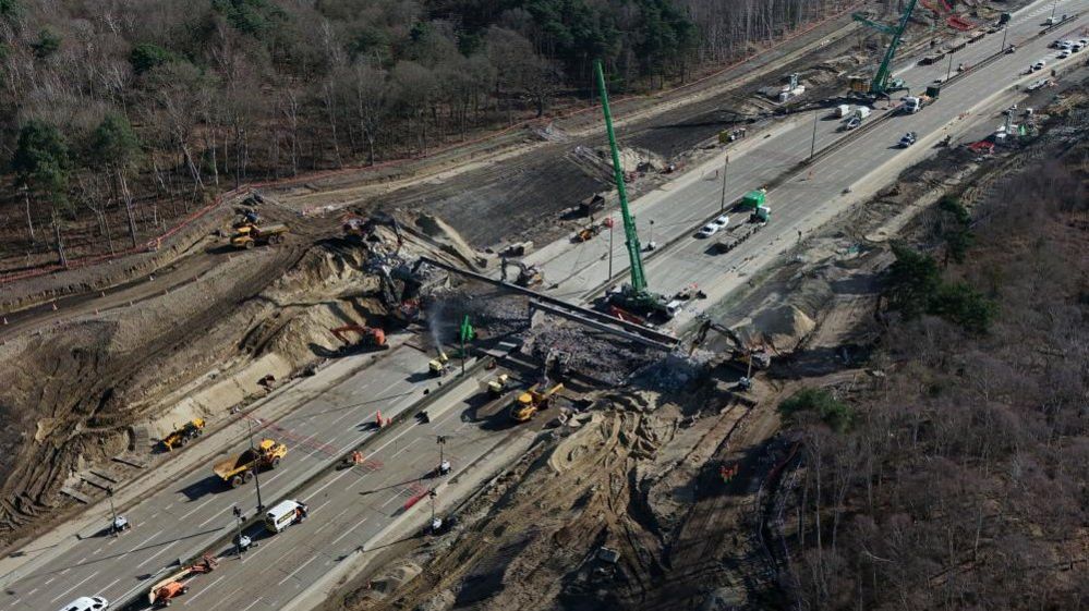 Cranes and vehicles surround a bridge that is being demolished on part of the M25