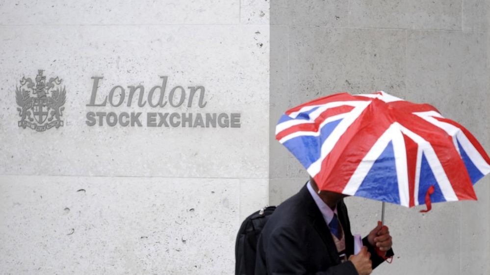 Человек с зонтиком проходит мимо Лондонской фондовой биржи