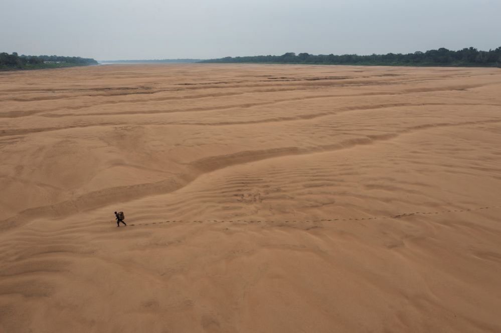 A fisherman walks across the dry bed of a branch of the Amazon River, Brazil, 13 October 2023