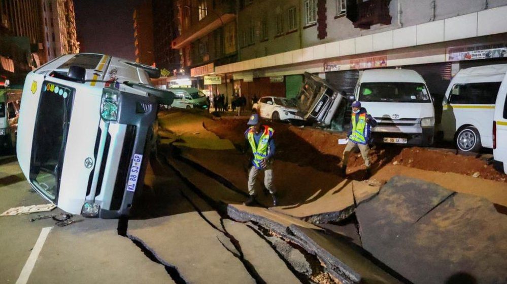 Полицейские осматривают поврежденные автомобили и дорогу после предполагаемого взрыва газа, в результате которого пострадали люди и был причинен значительный ущерб, в центральном деловом районе Йоханнесбурга, Южная Африка, 19 июля 2023 года.