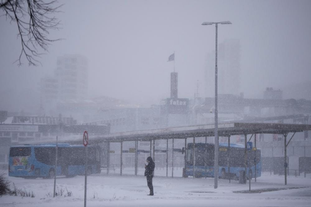 A person stands at a bus stop amid heavy snow in Randers, Denmark