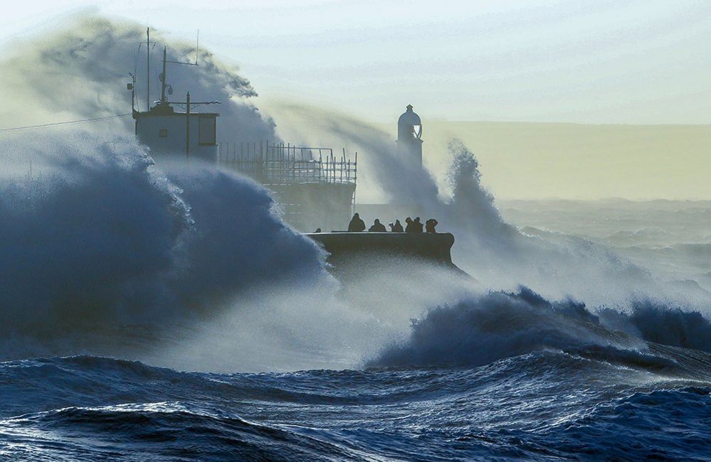 People look on as huge waves crash against the harbour wall in Porthcawl, South Wales