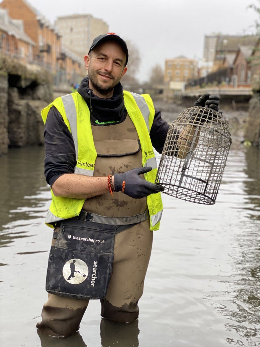 Simon Bourne, in full body waders, with a birdcage he found lying in the shallow water