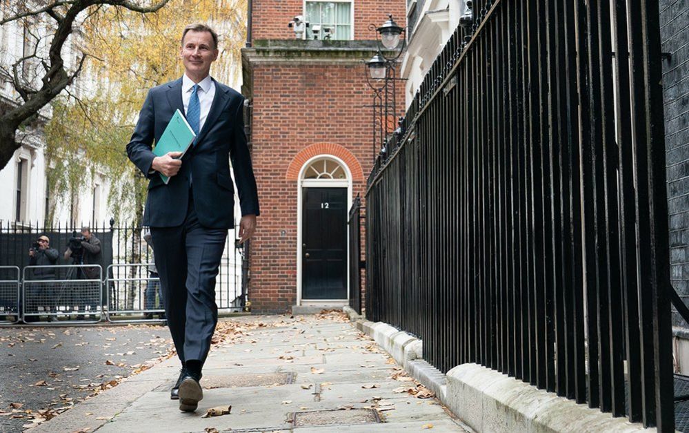 Jeremy Hunt walking outside number 11 Downing Street in a suit and blue tie holding a green budget statement in November 2023
