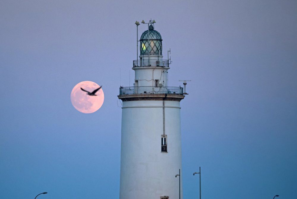 The buck moon rising in the sky over a lighthouse is seen at port of Malaga on 2 July
