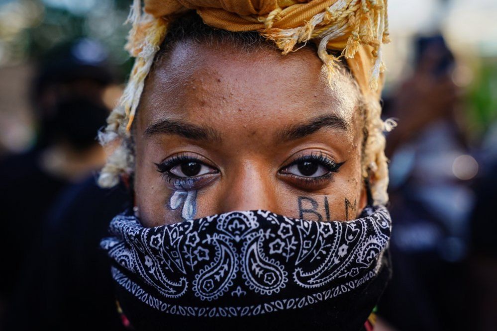 A woman with "BLM" written on her cheek poses during a demonstration