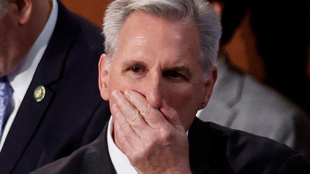 House Republican Leader Kevin McCarthy places his hand over his mouth as he stands inside the House Chamber