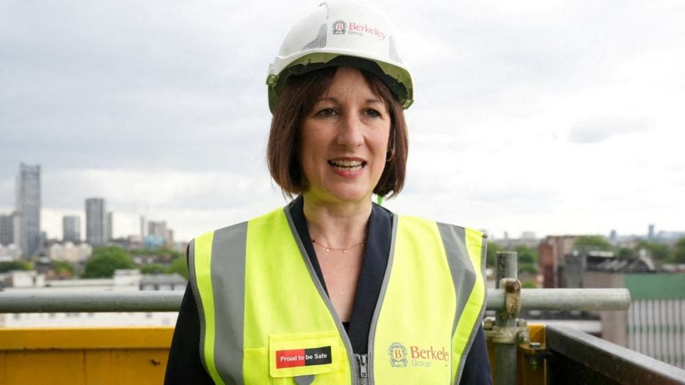 Rachel Reeves with dark hair wearing a white hard hat and a yellow hi-vis jacket