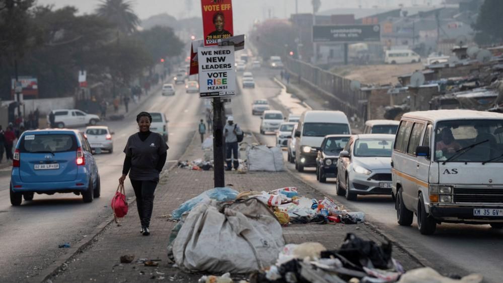 A woman walks past piles of uncollected trash in the township of Alexandra a day before the national election in Johannesburg, South Africa May 28, 2024
