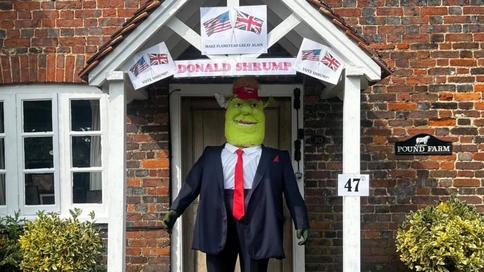 A Donald Trump scarecrow in the style of Shrek, a green creature, wearing a blue suit with a red tie, standing in the doorway of a house