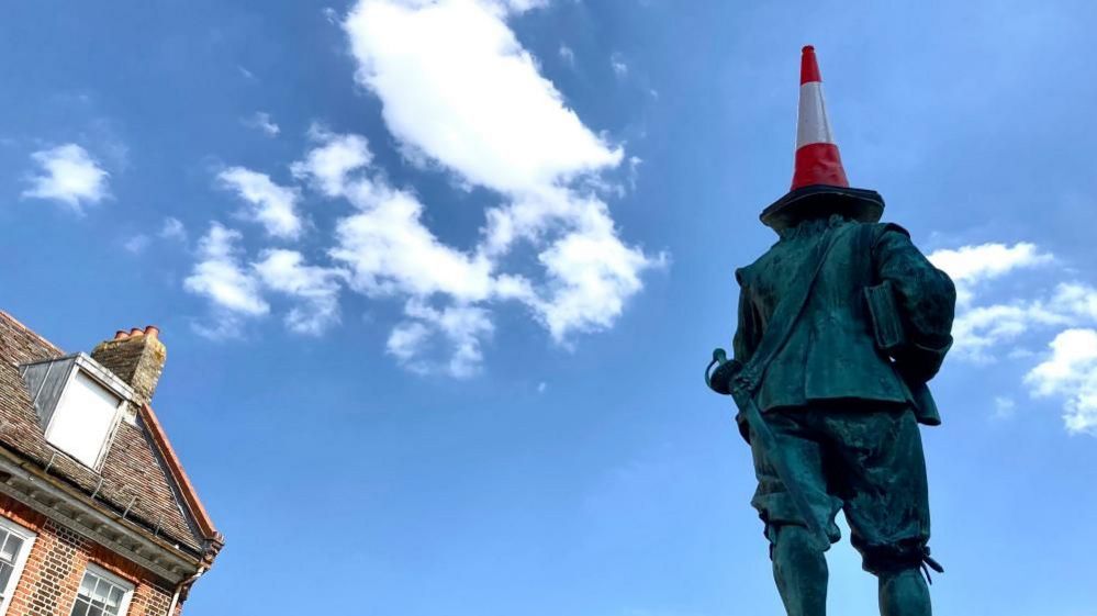 Rear view of Cromwell statue crowned with red and white traffic cone