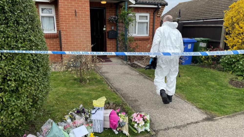 Flowers outside Joy Middleditch's bungalow with a forensics police officer about to enter the property