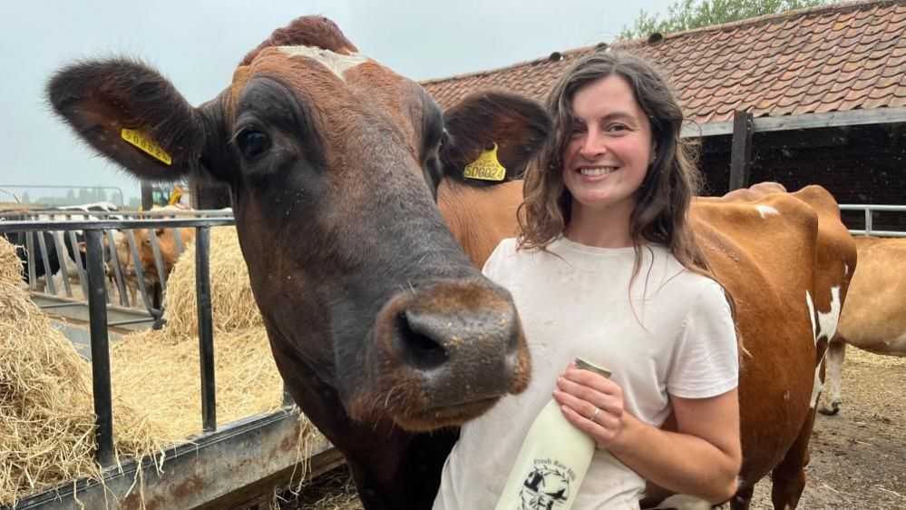 Erin Shreeve stroking a cow and holding a bottle of milk