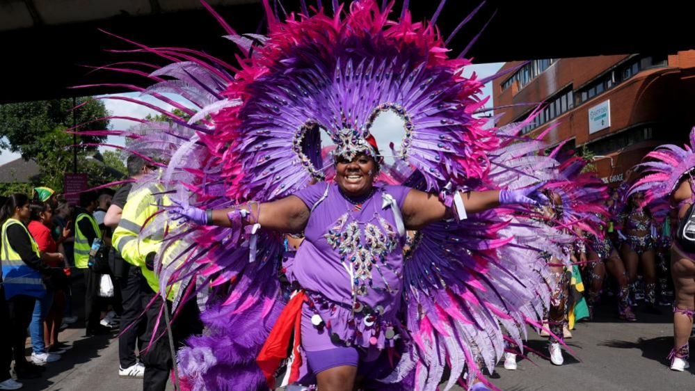 Notting Hill Carnival-goer celebrating in purple outfit with large decorative purple feathered wings on outfit