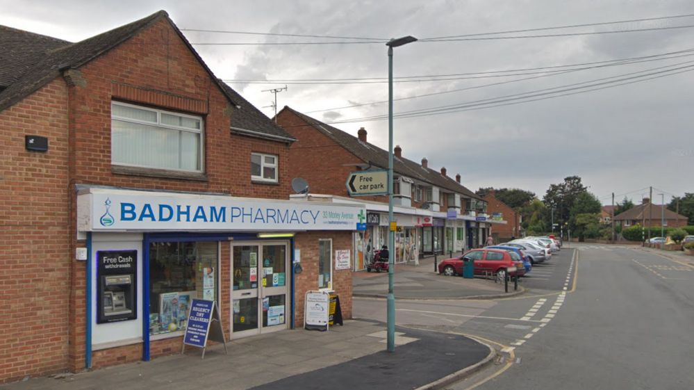Entrance to Badham Pharmacy with cars parked outside shops in the distance.
