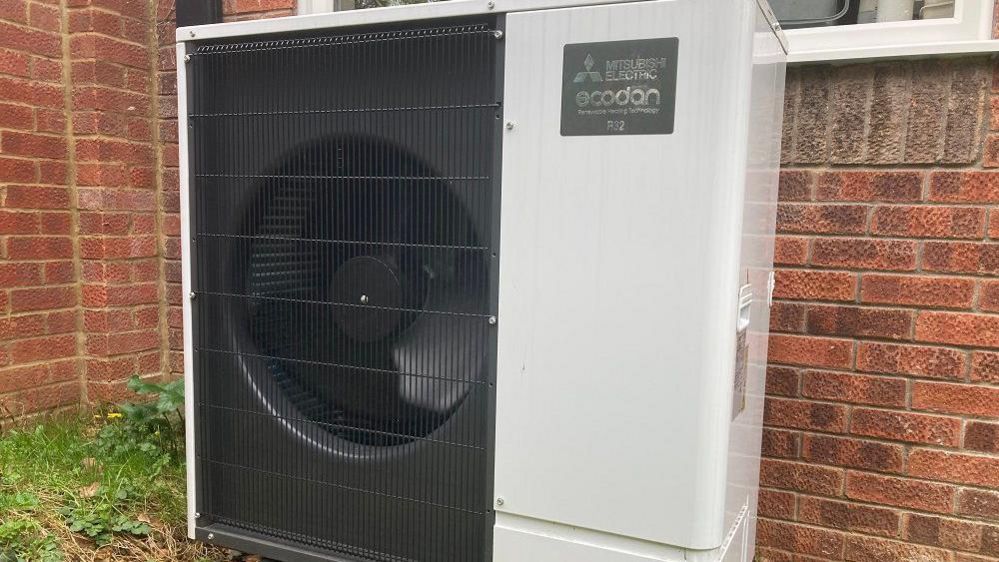 A close-up of a heat pump in a garden at the back of the house