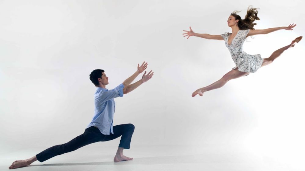 A male and a female ballet dancer with the female doing the splits in the air