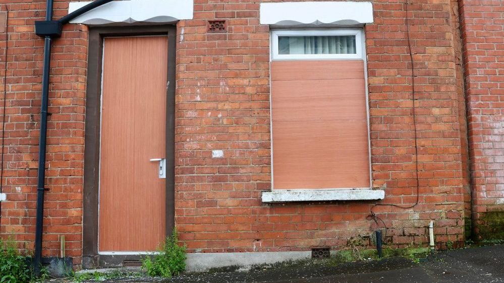 Red brick house in Belfast with door and windows boarded up after being attacked