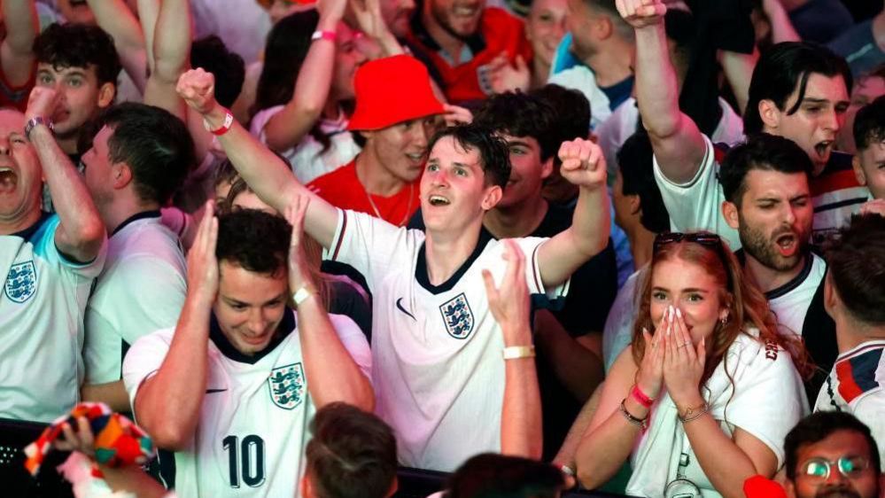 Happy fans celebrate, with arms raised in the air and some with hands over their face, looking happy and smiling