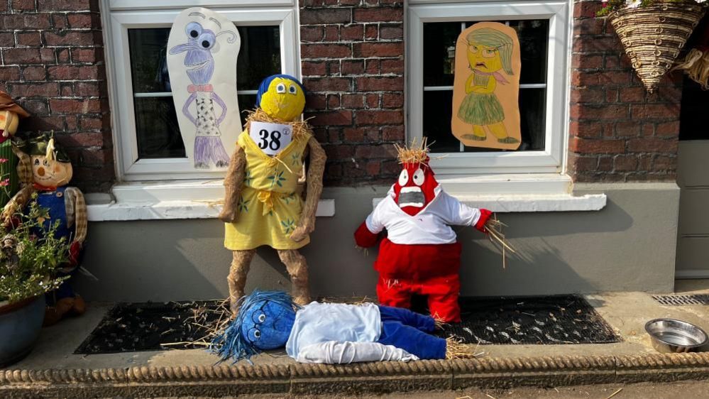 Characters from the Inside Out Disney films, as scarecrows, including Joy, in yellow, Anger, in red and Sadness, lying down