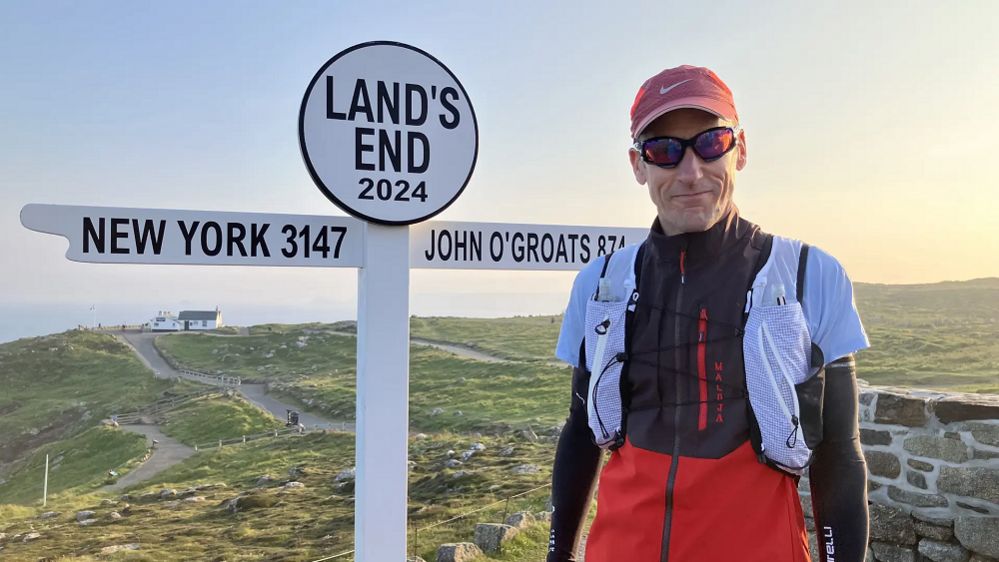 Martin Higgins looks at camera in running kit while standing next to Land's End sign