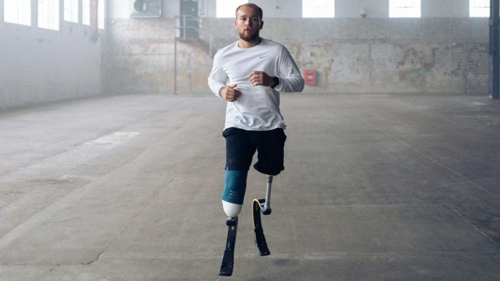 A male double amputee runs towards the camera with prosthetic legs.