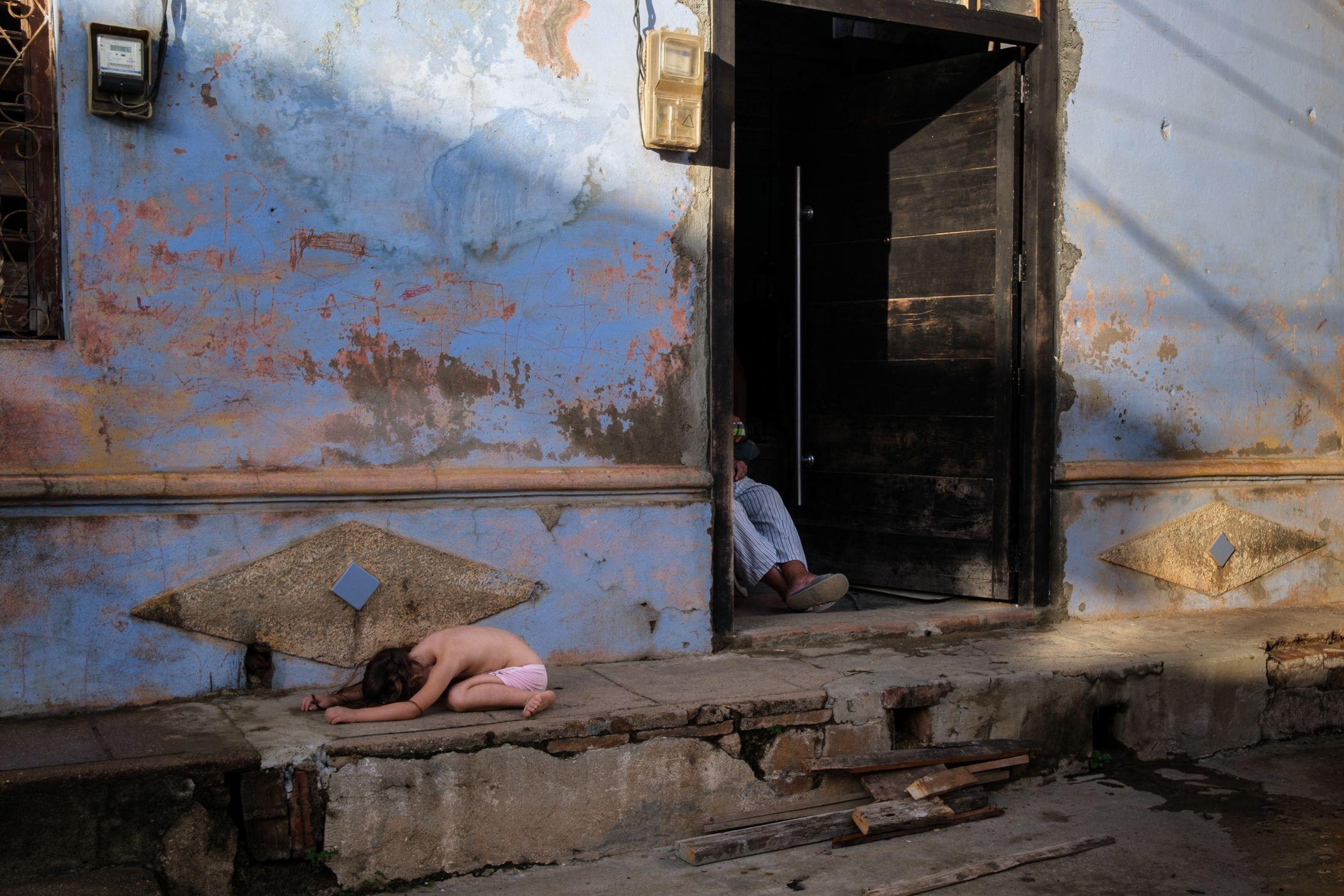 Una niña juega en la calle mientras su abuelo la cuida en Trinidad, Cuba. 