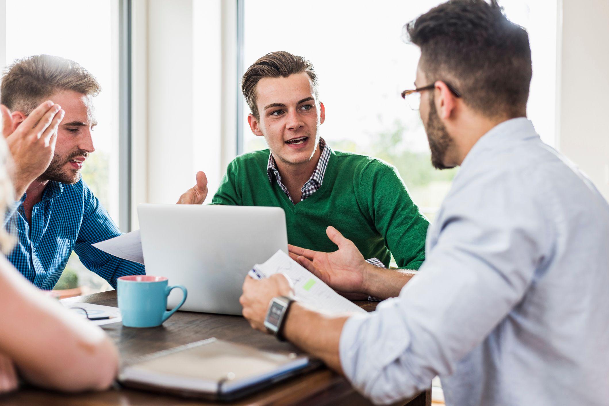 Três homens jovens discutindo durante reunião de trabalho