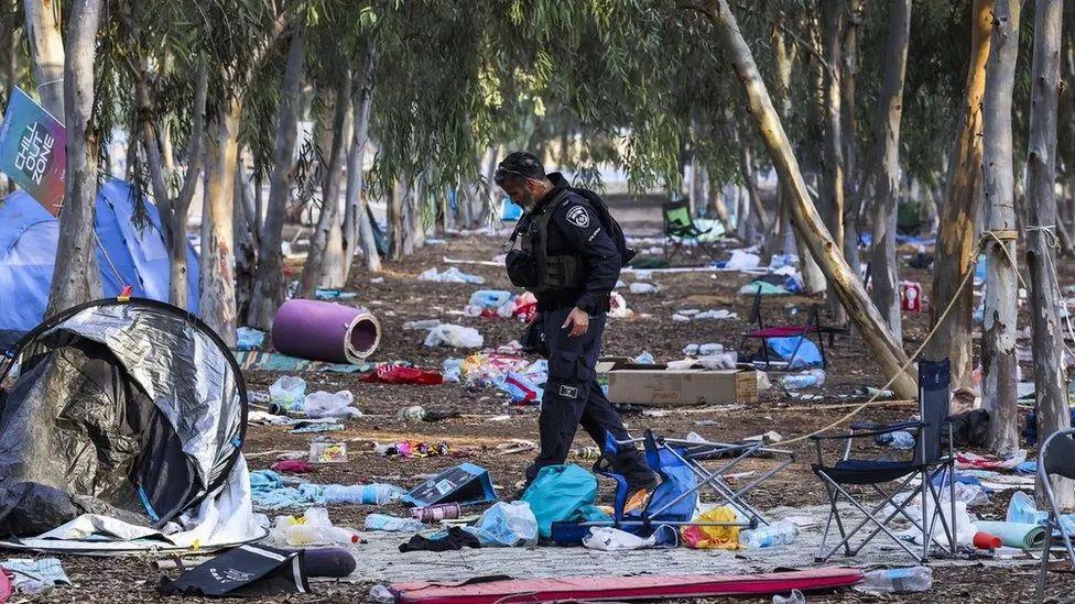 Policial caminhando pelo local onde foi realizado o festival de música, em meio a lixo, restos de barracas e colchonetes