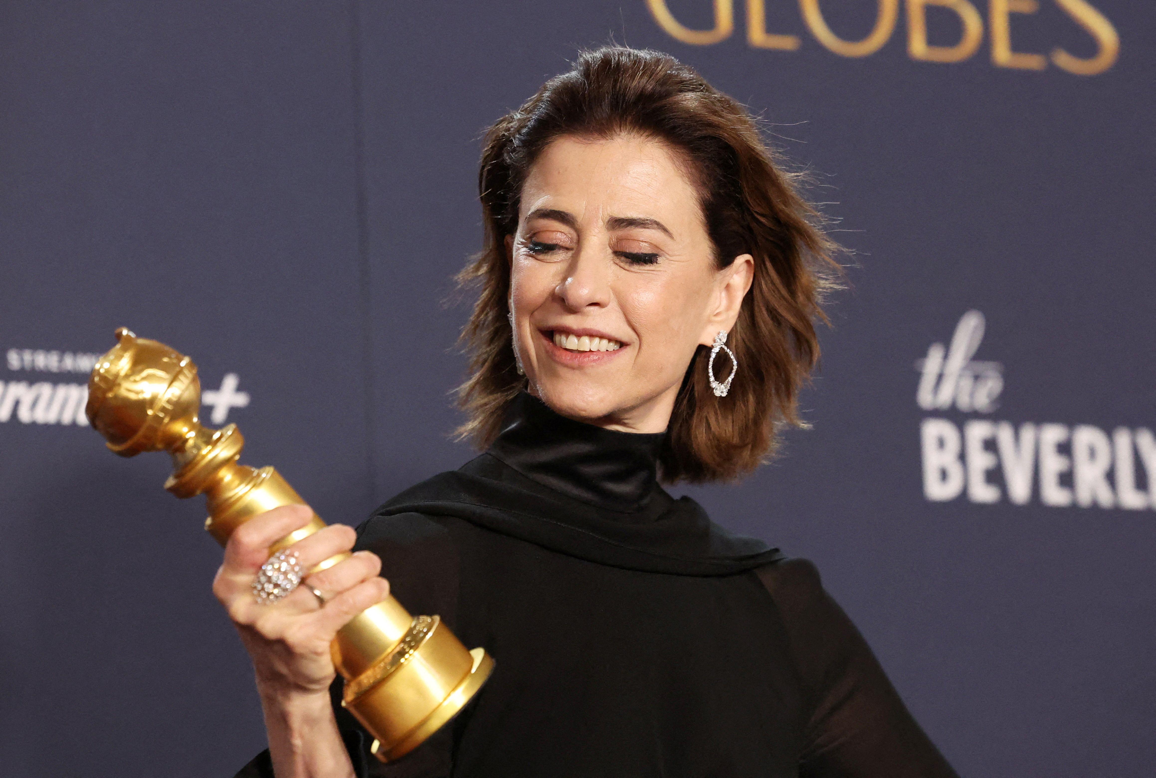 Fernanda Torres sorrindo ao olhar troféu do Globo de Ouro