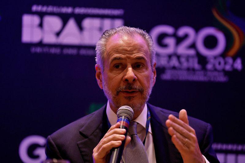 André Corrêa do Lago com microfone na mão em evento do G20 com banner atrás de si 
