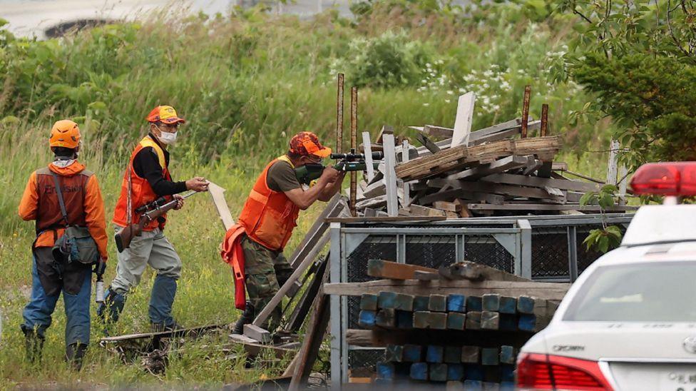 Caçadores com espingardas atiram atrás de proteção