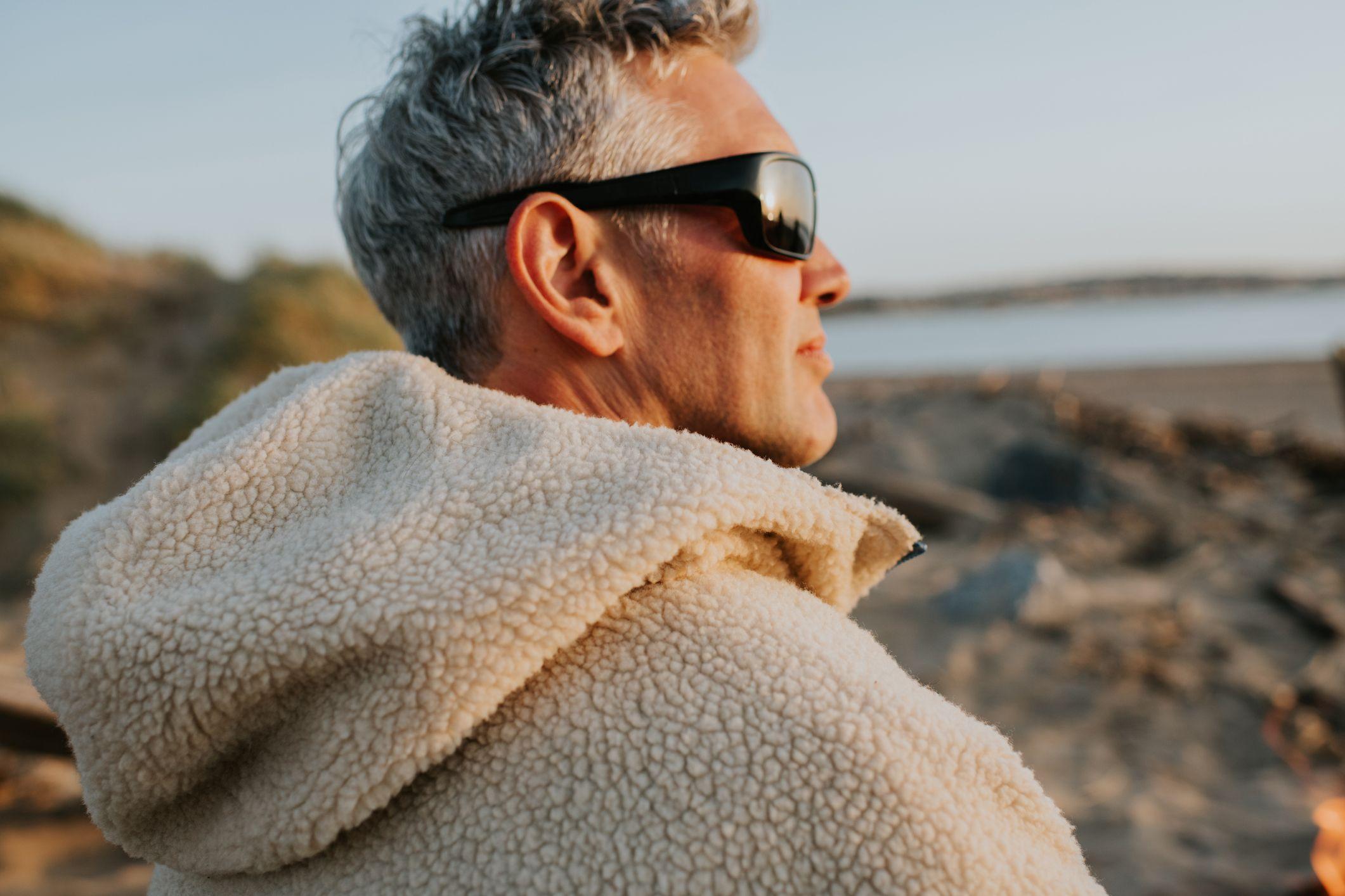 رجل يقف على الشاطئ تحت ضوء الشمس قبل الغروب، ويرتدي نظارة شمسية لحماية عينيه.