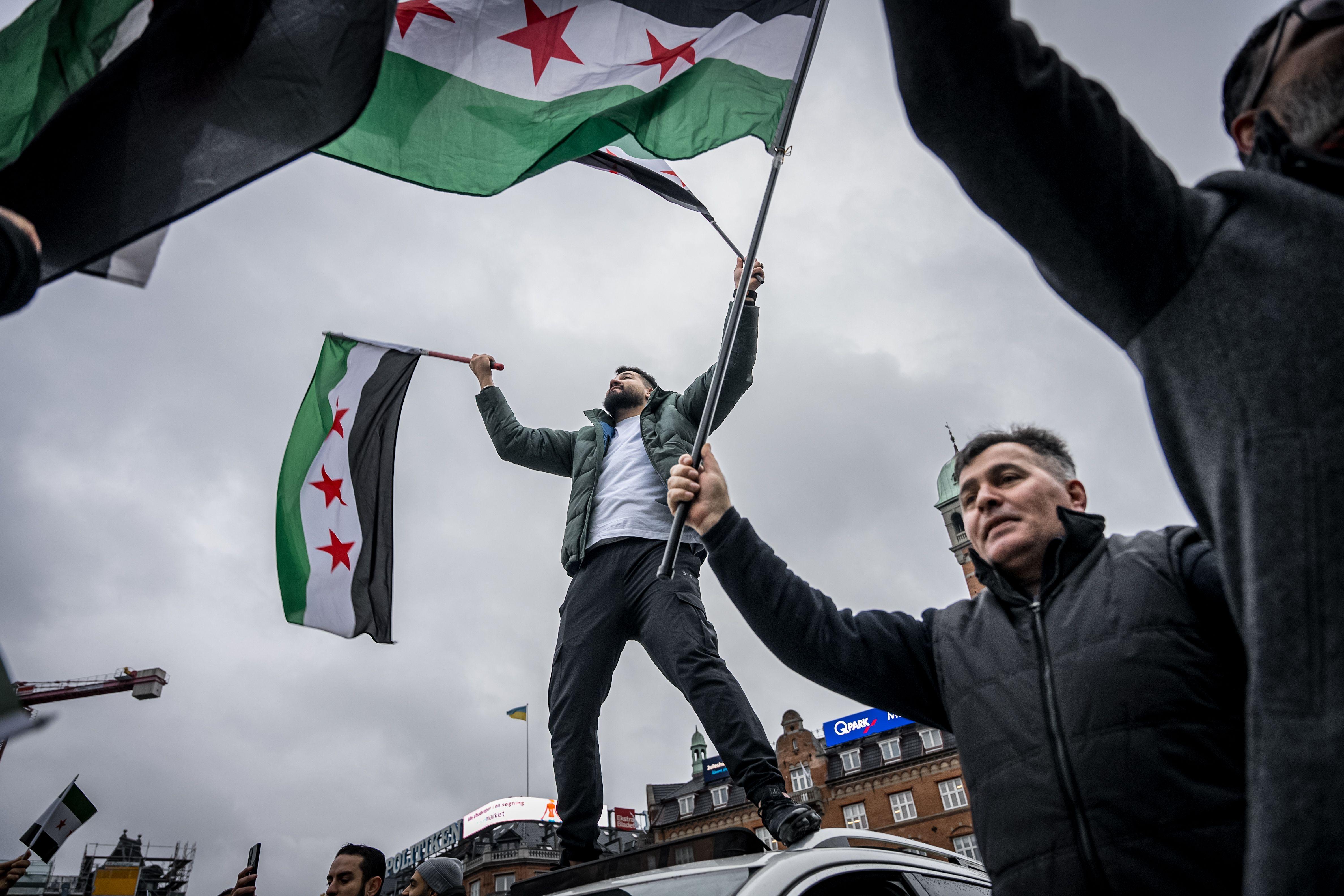 Personas y miembros de la Asociación Siria en Dinamarca llevan banderas de la oposición siria mientras celebran la toma rebelde de Damasco, en Copenhague, Dinamarca.