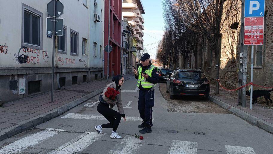 Devojka u zelenom prsluku sa ružama u rukama i policajac