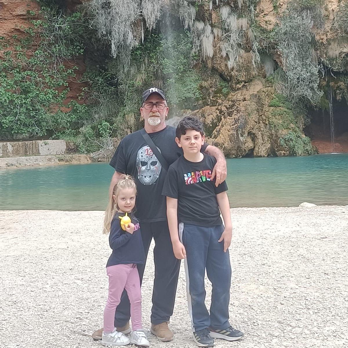 Francisco con sus nietos, están abrazados y de pie frente a un paisaje natural.