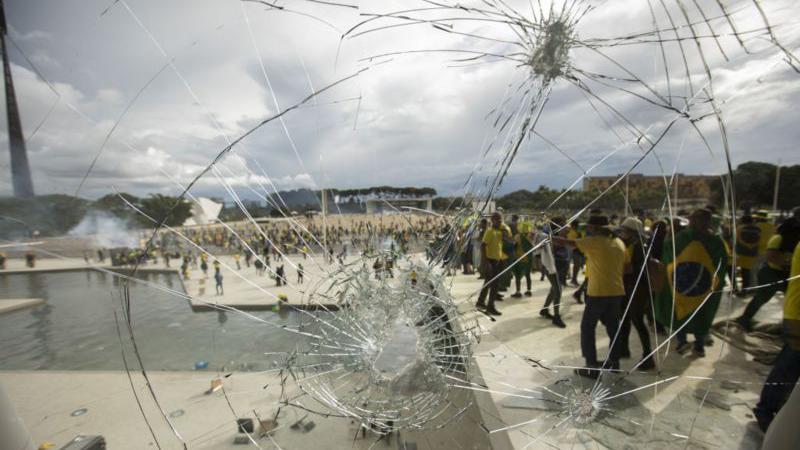 vidro quebrado no STF com manifestantes ao fundo em 8 de janeiro de 2023