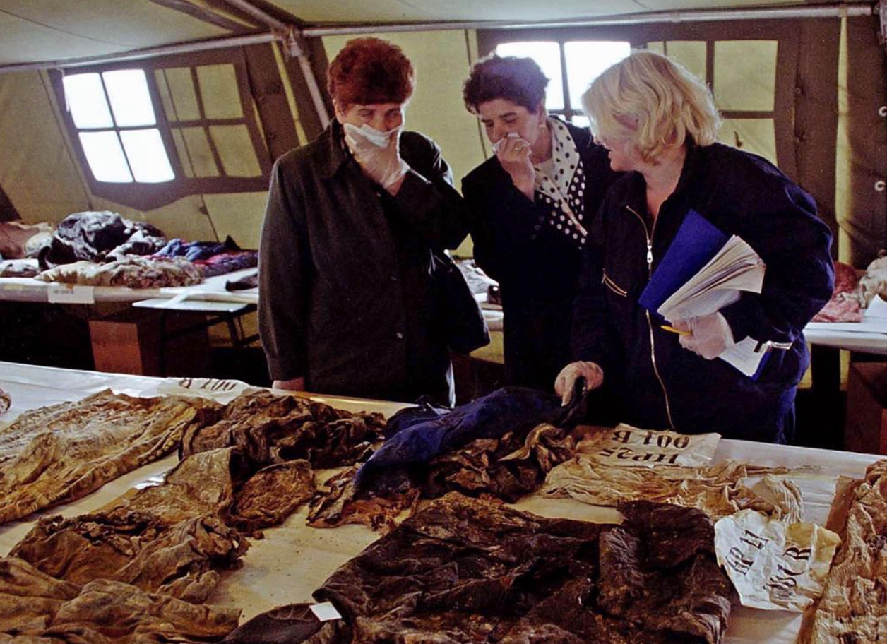 Tres mujeres examinan restos hallados en fosas comunes mientras dos de ellas se tapan la nariz.
