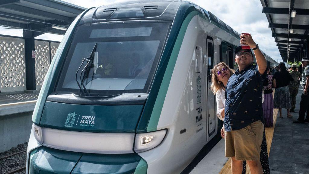 Pasajeros junto a un convoy del Tren Maya