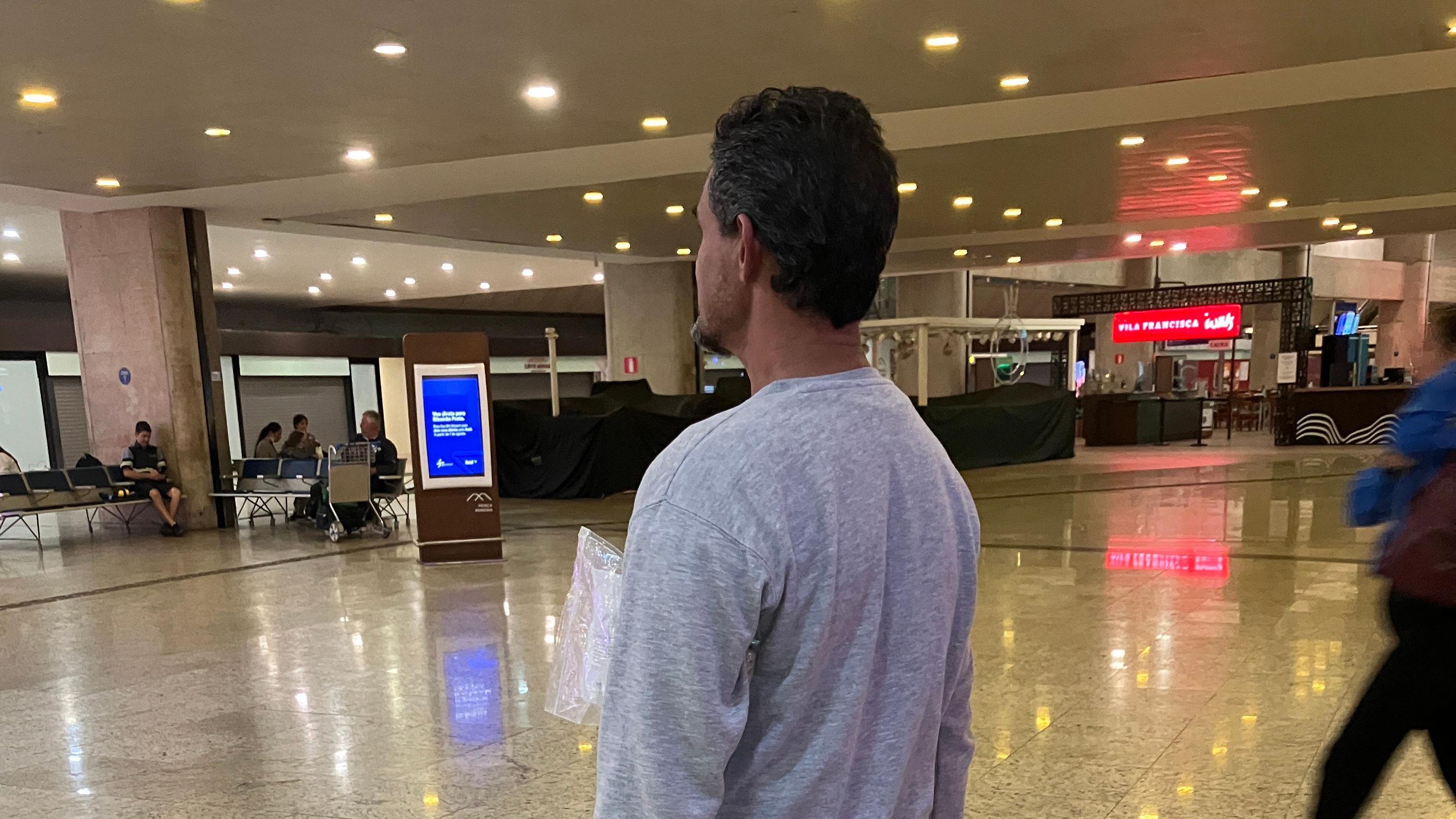 Foto de um homem de perfil em um saguão de aeroporto. 