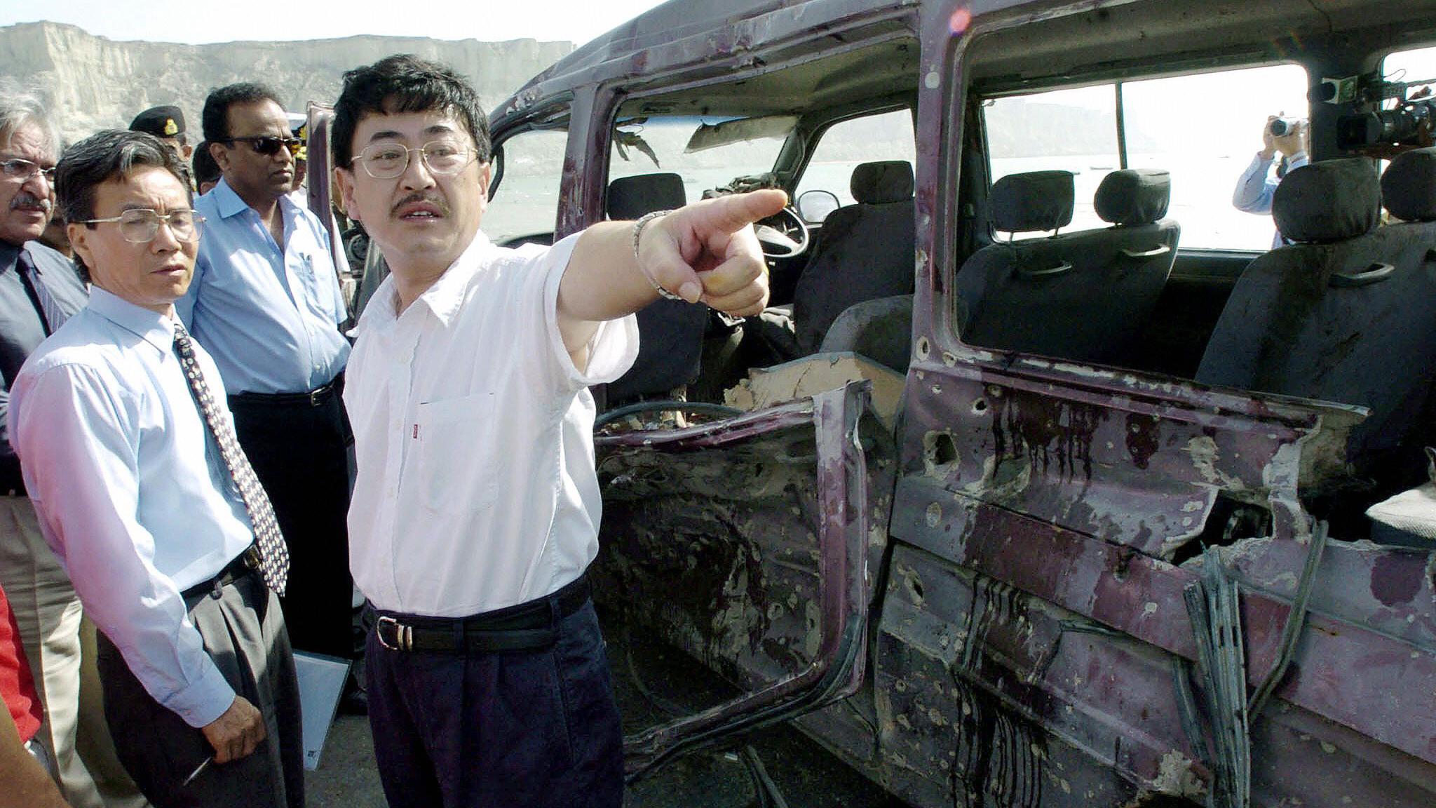 Trabajadores chinos junto a los restos de un vehículo que transportaba ciudadanos chinos y fue atacado por militantes paquistaníes en 2004